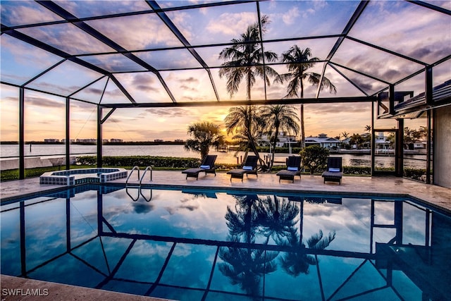 pool at dusk with a water view, an in ground hot tub, a lanai, and a patio