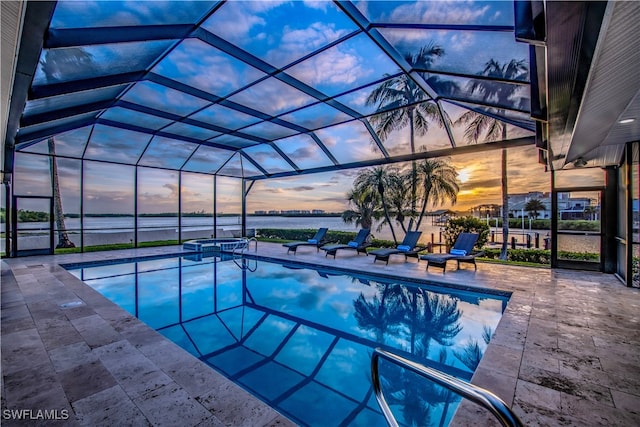 pool at dusk featuring a water view, a patio area, and a lanai