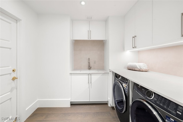 clothes washing area featuring dark wood-type flooring, washing machine and dryer, cabinets, and sink