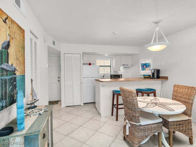 kitchen featuring kitchen peninsula, hanging light fixtures, white cabinets, white fridge, and light tile patterned floors