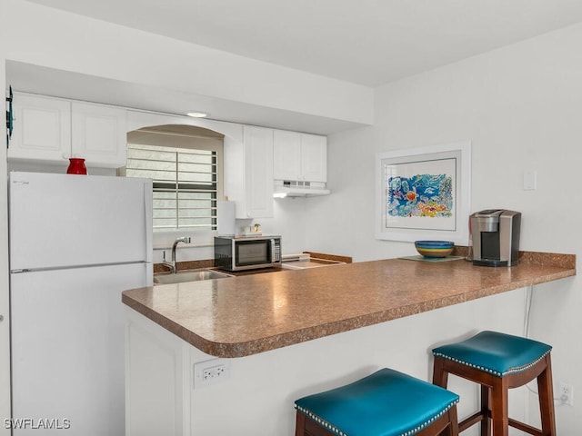 kitchen featuring sink, white cabinets, a kitchen breakfast bar, and white refrigerator