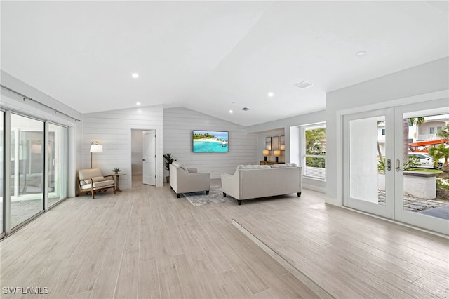 unfurnished living room featuring wooden walls, vaulted ceiling, light wood-type flooring, and french doors