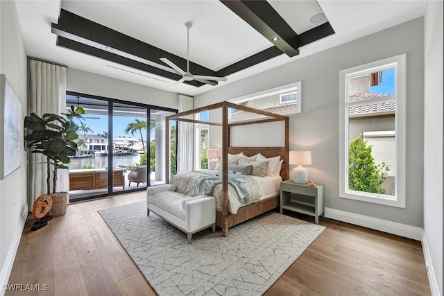 bedroom featuring hardwood / wood-style floors, access to outside, ceiling fan, a water view, and beam ceiling