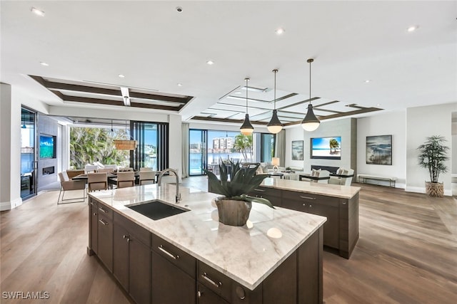 kitchen with decorative light fixtures, a spacious island, sink, light stone counters, and light hardwood / wood-style flooring