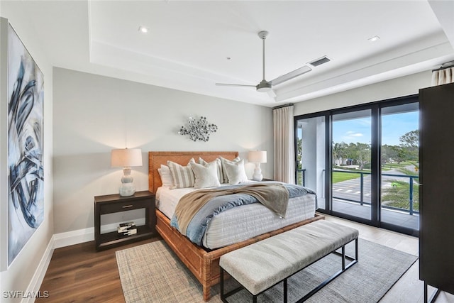 bedroom featuring ceiling fan, a tray ceiling, dark hardwood / wood-style flooring, and access to outside