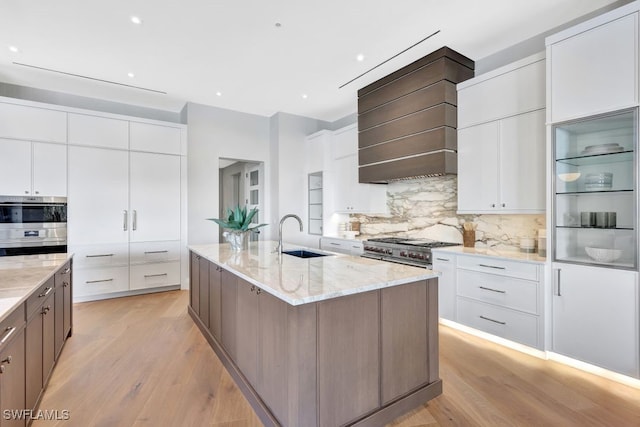 kitchen featuring a spacious island, custom exhaust hood, white cabinetry, stainless steel appliances, and light stone countertops