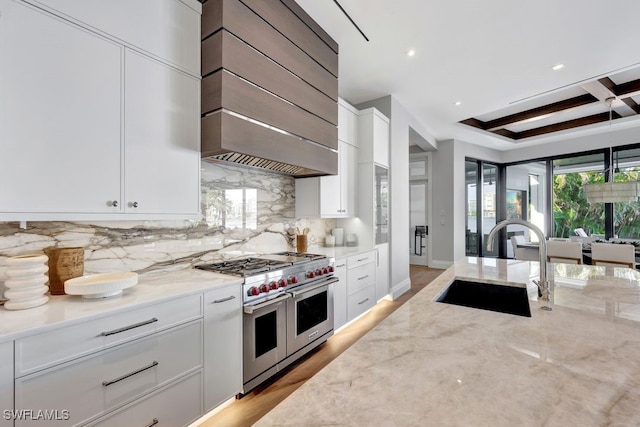 kitchen with coffered ceiling, sink, white cabinetry, light stone counters, and double oven range