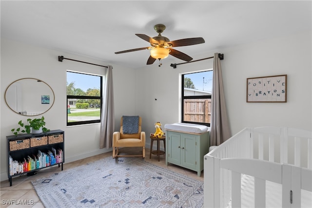 bedroom featuring a nursery area, light tile patterned flooring, multiple windows, and ceiling fan