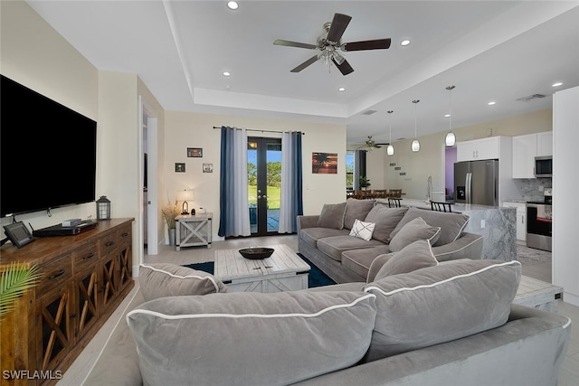 living room with a tray ceiling, ceiling fan, and french doors