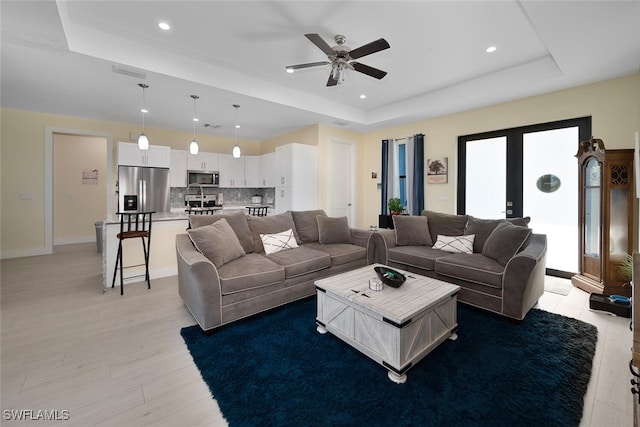 living room featuring french doors, light wood-type flooring, a tray ceiling, and ceiling fan