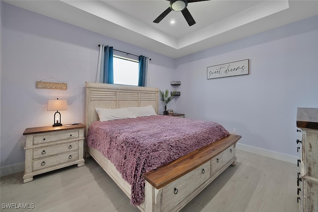 bedroom with a raised ceiling, ceiling fan, and light wood-type flooring