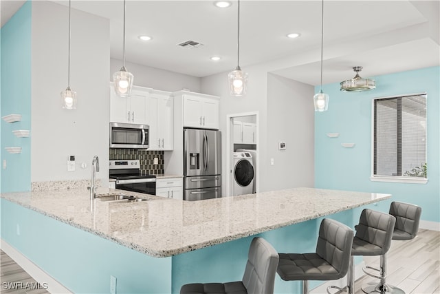 kitchen with white cabinetry, pendant lighting, appliances with stainless steel finishes, and washer / clothes dryer