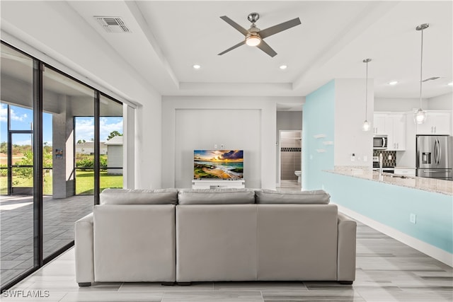 living room featuring ceiling fan, a tray ceiling, and sink