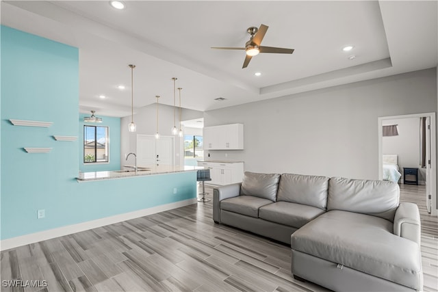 living room with ceiling fan, a raised ceiling, light hardwood / wood-style flooring, and sink