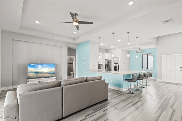 living room featuring ceiling fan, light hardwood / wood-style floors, a tray ceiling, and washer / clothes dryer