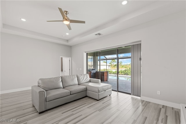 living room featuring ceiling fan, light hardwood / wood-style floors, and a raised ceiling