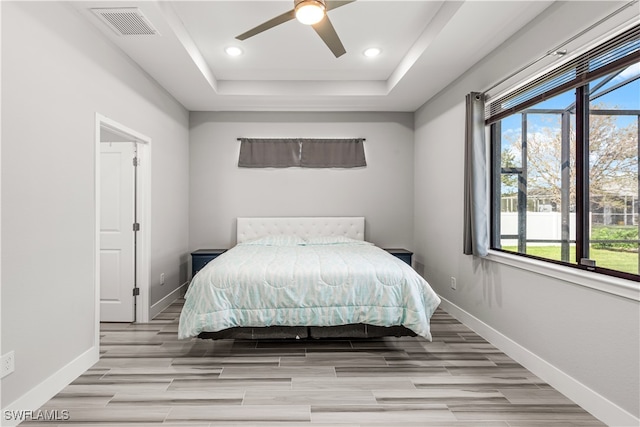 bedroom with ceiling fan, light hardwood / wood-style flooring, and a tray ceiling