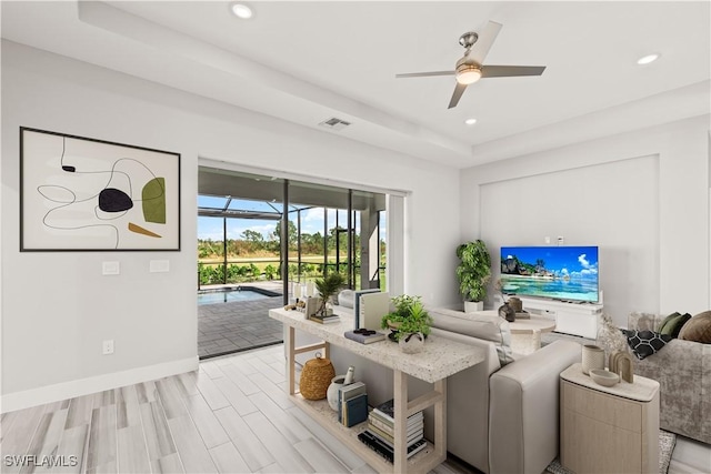 living room with ceiling fan, light hardwood / wood-style floors, and a raised ceiling