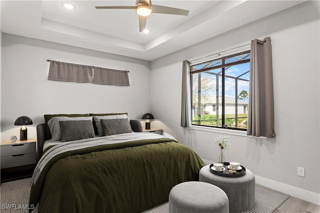 bedroom featuring ceiling fan, wood-type flooring, and a raised ceiling