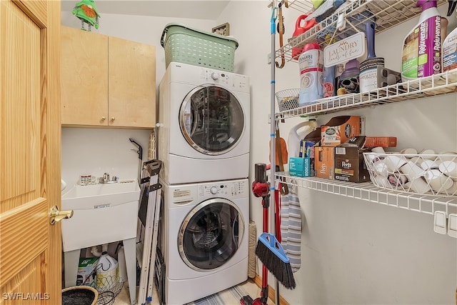 laundry area featuring cabinets, stacked washer / dryer, and sink