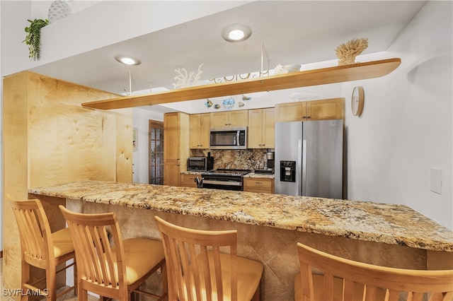 kitchen featuring appliances with stainless steel finishes, kitchen peninsula, decorative backsplash, a breakfast bar area, and light brown cabinets