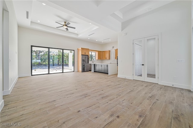 unfurnished living room featuring light hardwood / wood-style floors, a raised ceiling, a towering ceiling, and ceiling fan