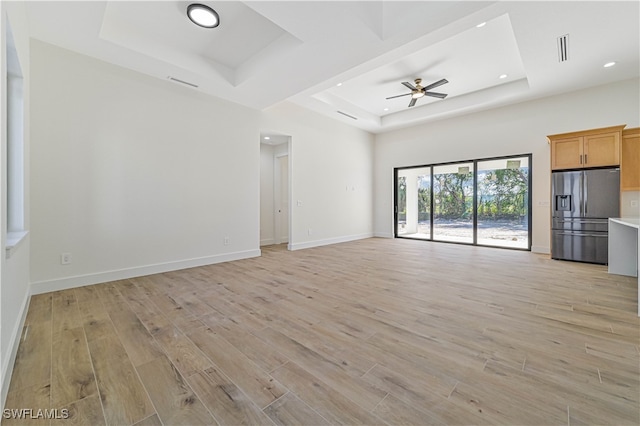 unfurnished living room featuring ceiling fan, light wood-type flooring, and a raised ceiling