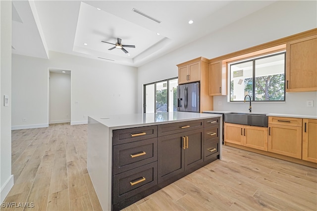 kitchen with a kitchen island, a tray ceiling, sink, stainless steel fridge with ice dispenser, and light wood-type flooring