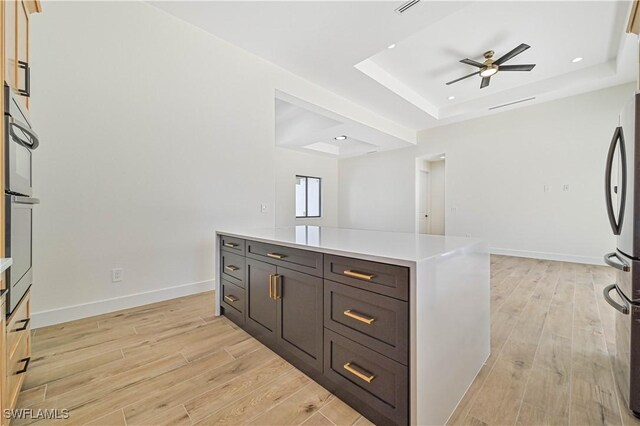 kitchen with a kitchen island, a tray ceiling, ceiling fan, stainless steel refrigerator, and light hardwood / wood-style flooring