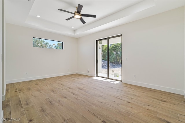 spare room with light hardwood / wood-style floors, ceiling fan, and a raised ceiling