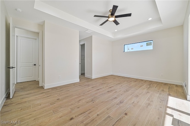 unfurnished room with a tray ceiling, light wood-type flooring, and ceiling fan