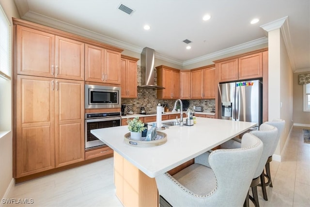 kitchen featuring stainless steel appliances, light countertops, a kitchen island with sink, and wall chimney range hood