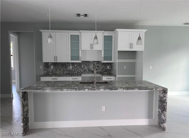 kitchen featuring an island with sink, white cabinetry, dark stone counters, pendant lighting, and decorative backsplash