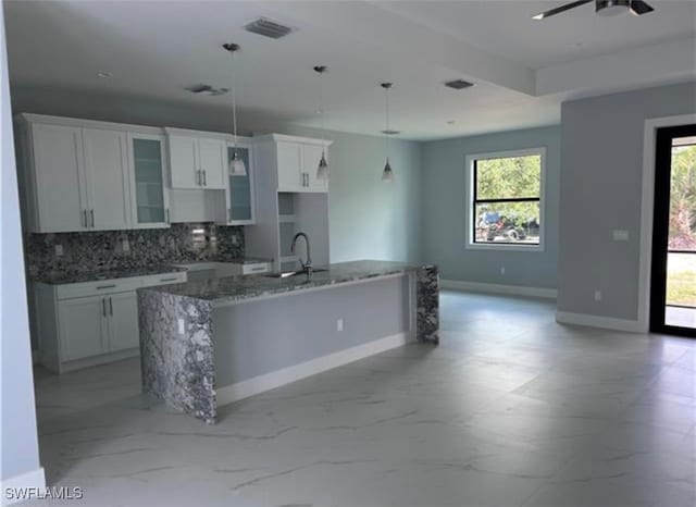 kitchen featuring stone counters, white cabinets, a center island with sink, and backsplash