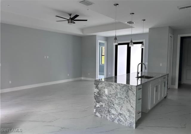 kitchen featuring stone counters, decorative light fixtures, an island with sink, sink, and white cabinets