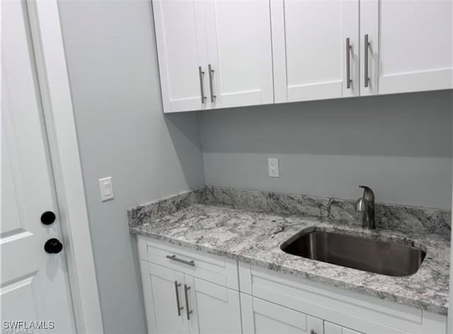 kitchen featuring light stone counters, sink, and white cabinets