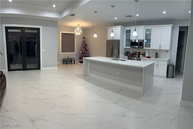 kitchen with sink, white cabinetry, decorative light fixtures, appliances with stainless steel finishes, and a kitchen island with sink