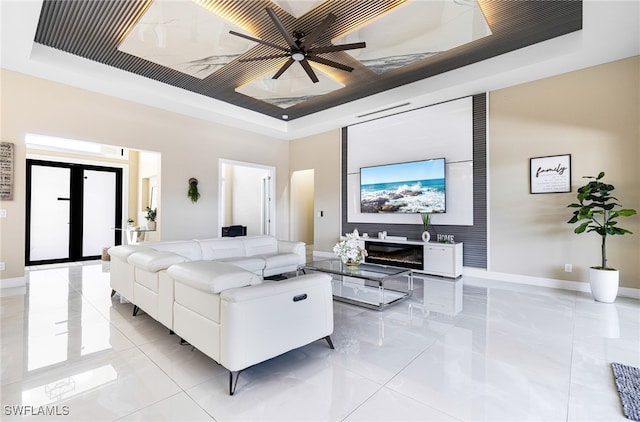 living room featuring ceiling fan, light tile patterned floors, a raised ceiling, a fireplace, and french doors