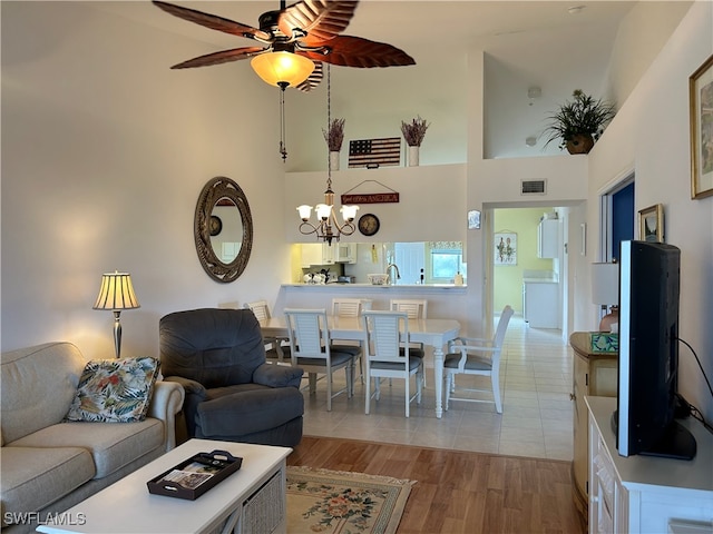 living room featuring high vaulted ceiling, light wood-type flooring, and ceiling fan with notable chandelier