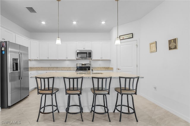 kitchen featuring appliances with stainless steel finishes, decorative light fixtures, white cabinetry, and an island with sink