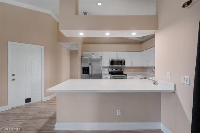 kitchen with white cabinetry, stainless steel appliances, light hardwood / wood-style flooring, kitchen peninsula, and ornamental molding