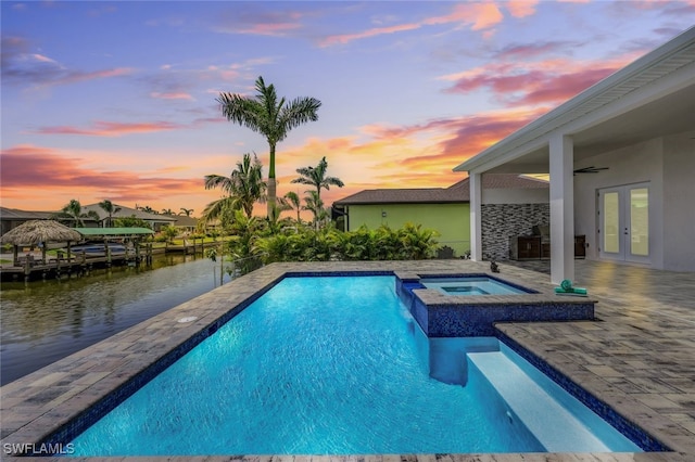 pool at dusk with french doors, an in ground hot tub, a water view, a patio, and ceiling fan