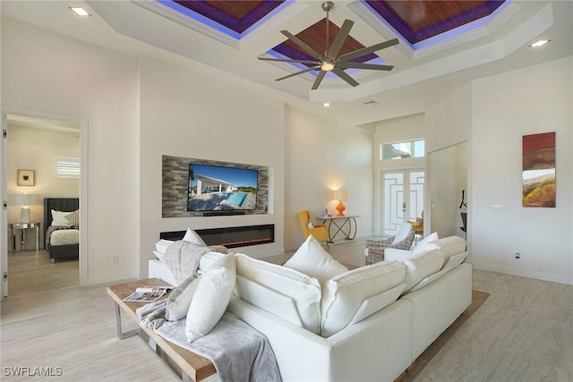 living room featuring light wood-type flooring, ceiling fan, coffered ceiling, beamed ceiling, and a high ceiling