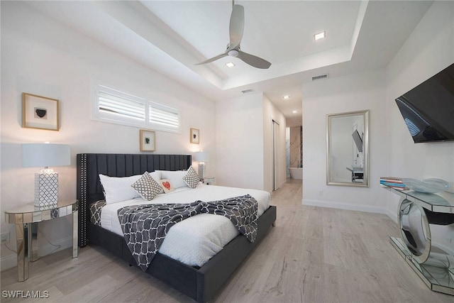 bedroom with connected bathroom, a tray ceiling, light hardwood / wood-style floors, and ceiling fan