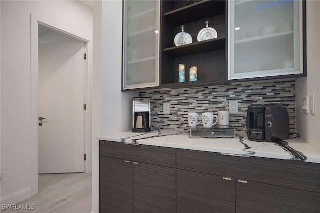 bar featuring light hardwood / wood-style flooring, light stone countertops, dark brown cabinets, and backsplash