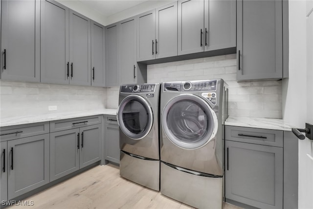 clothes washing area featuring light hardwood / wood-style flooring, cabinets, and washer and clothes dryer