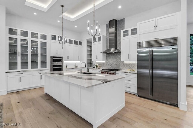 kitchen featuring sink, an island with sink, light hardwood / wood-style floors, stainless steel appliances, and wall chimney exhaust hood