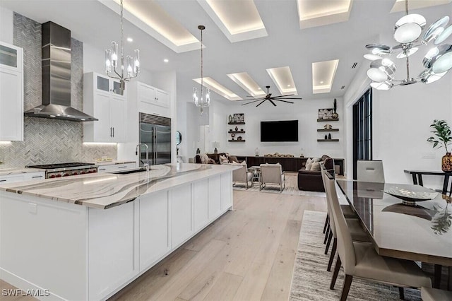 kitchen with a spacious island, white cabinets, wall chimney range hood, and stainless steel appliances