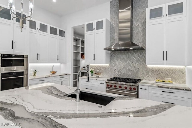 kitchen with wall chimney exhaust hood, appliances with stainless steel finishes, light stone counters, and white cabinets