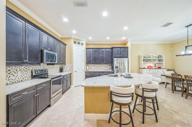 kitchen featuring crown molding, appliances with stainless steel finishes, light tile patterned floors, and an island with sink